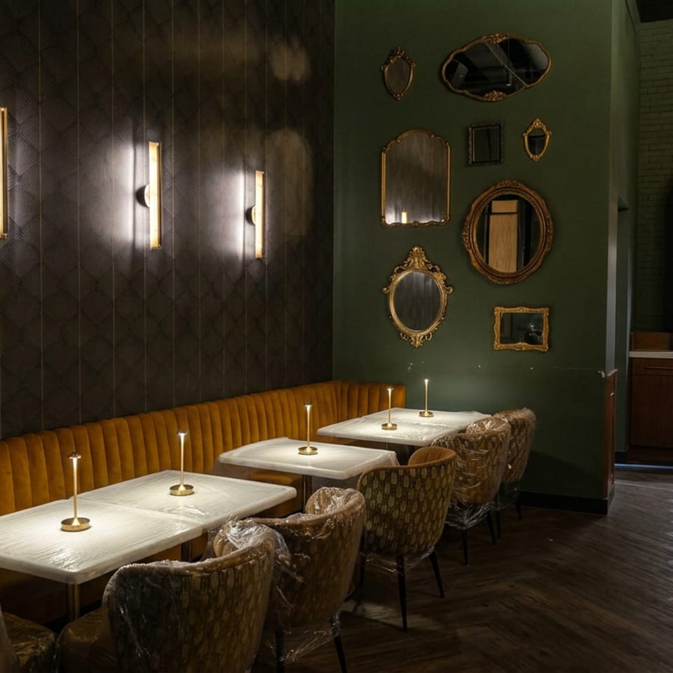 Elegant restaurant dining area with mustard banquette seating, candlelit tables, patterned chairs, decorative mirrors, and illuminated bar shelves.