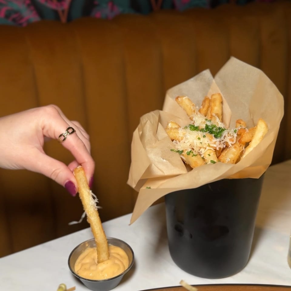 Glossy slider burgers sit beside truffle fries with Parmesan and herbs, dipping sauce, and a hand holding one fry.